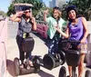 Three people are posing with two on Segways and one taking a selfie all smiling and having a good time near a fountain and yacht