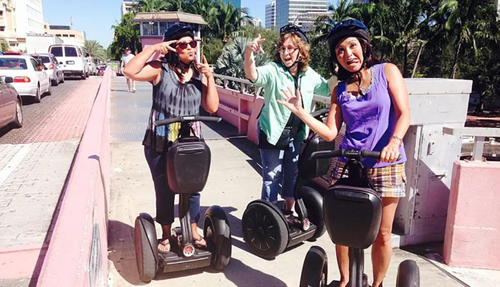 Three people are posing for a photo while standing on Segways on a sunny day making playful hand gestures and wearing helmets for safety