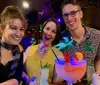 Three cheerful friends pose with colorful tropical drinks at a bar