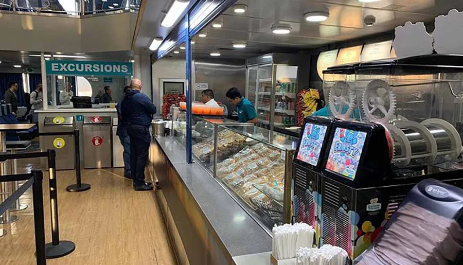 A person is standing before a counter labeled EXCURSIONS inside a ferry or cruise ship, with a cafeteria setup visible and crew members in the background.