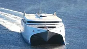 The image shows a modern, high-speed catamaran ferry cutting through the water, leaving a wake behind.