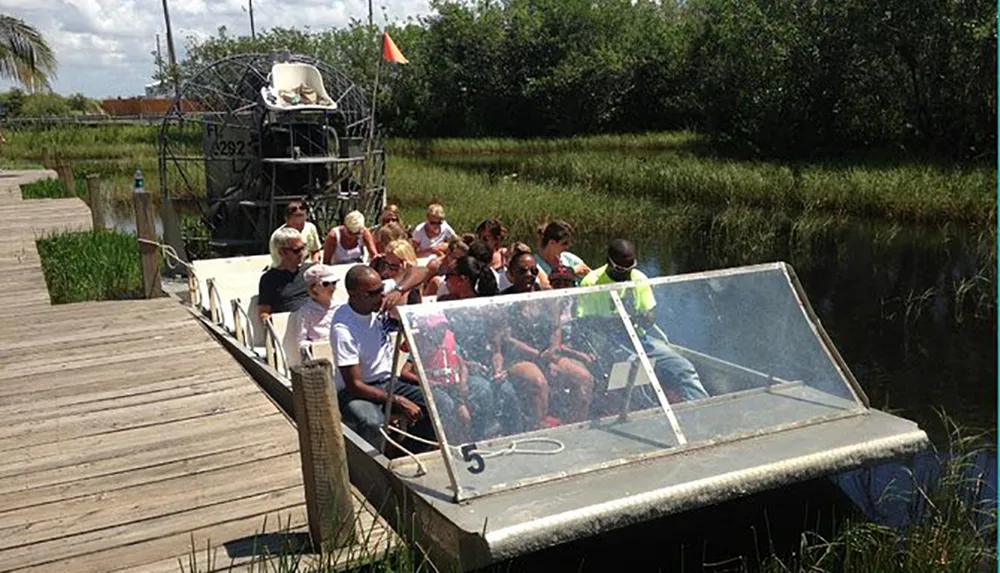 A group of passengers is seated in an airboat preparing for a tour in a marshy area