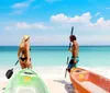 A man and a woman are preparing colorful kayaks on a sunny beach with clear turquoise waters