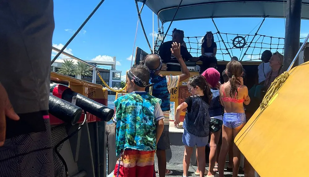 Children are gathered on what appears to be the deck of a themed boat engaging with a person dressed as a pirate who is speaking to them