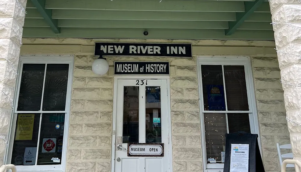 The image shows the entrance to the New River Inn which is a Museum of History indicated by the signs above the door with informational posters and a welcome sign on the porch