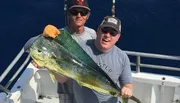 Two men are posing on a boat with a large fish they have caught.