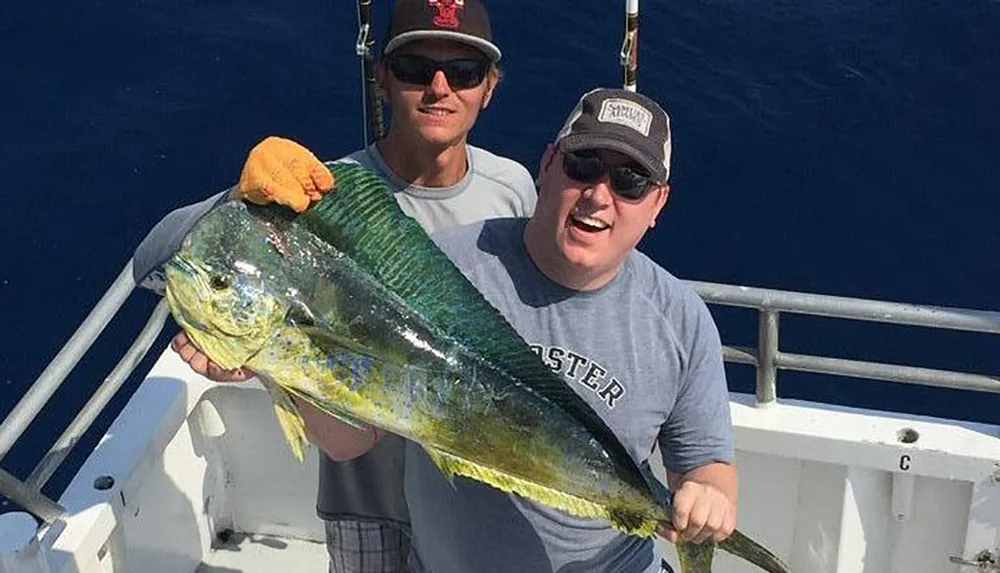 Two men are posing on a boat with a large fish they have caught