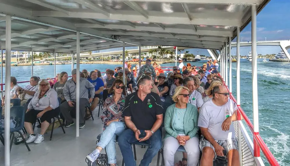 A group of people is seated on a covered boat enjoying a sightseeing tour on a sunny day