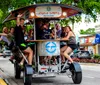 A group of people are enjoying a ride on a multi-person pedal-powered vehicle known as a pedal pub or party bike on a city street