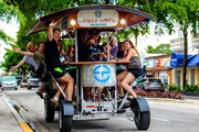 A group of people are enjoying a ride on a multi-person pedal-powered vehicle, known as a pedal pub or party bike, on a city street.