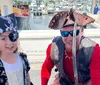 A group of children dressed as pirates and sporting eye patches and bandanas are joyfully engaging in a themed activity with one girl triumphantly raising her fist and holding a toy sword