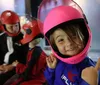 Three individuals in full-body suits and helmets are indoors skydiving in a vertical wind tunnel with an onlooker visible in the background