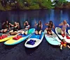 A group of cheerful people are posing on paddleboards on a calm water surface surrounded by natural scenery