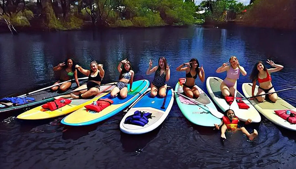 A group of cheerful people are posing on paddleboards on a calm water surface surrounded by natural scenery