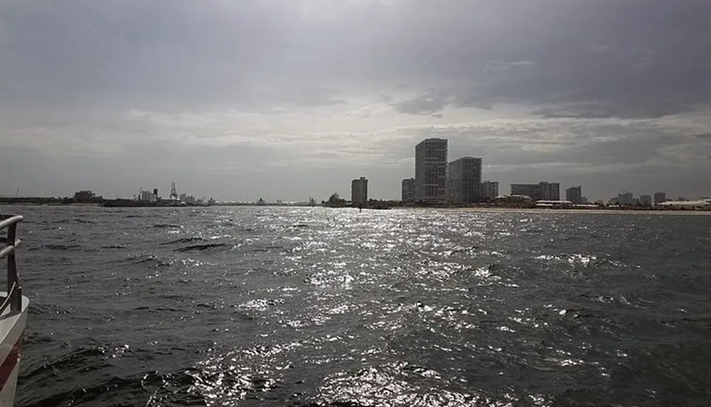 A view from a boat showing choppy waters with a city skyline under a cloudy sky