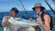 Two individuals are posing with a large fish on a boat, showcasing their catch with cheerful expressions.