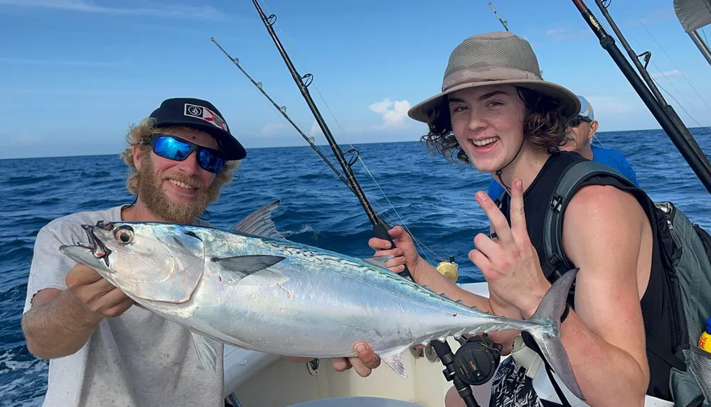 Two individuals are posing with a large fish on a boat showcasing their catch with cheerful expressions