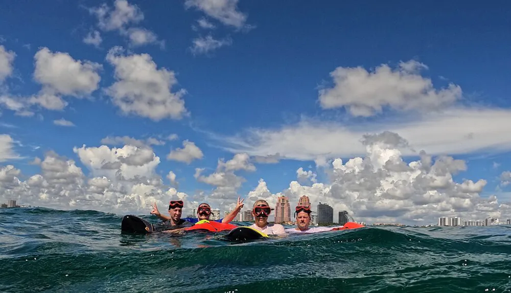 A group of people wearing life jackets and snorkeling gear are floating on the ocean with a city skyline and a bright cloudy sky in the background