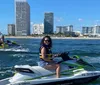 Three pairs of people are riding jet skis on a waterway with waterfront houses and buildings in the background