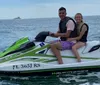 Three pairs of people are riding jet skis on a waterway with waterfront houses and buildings in the background