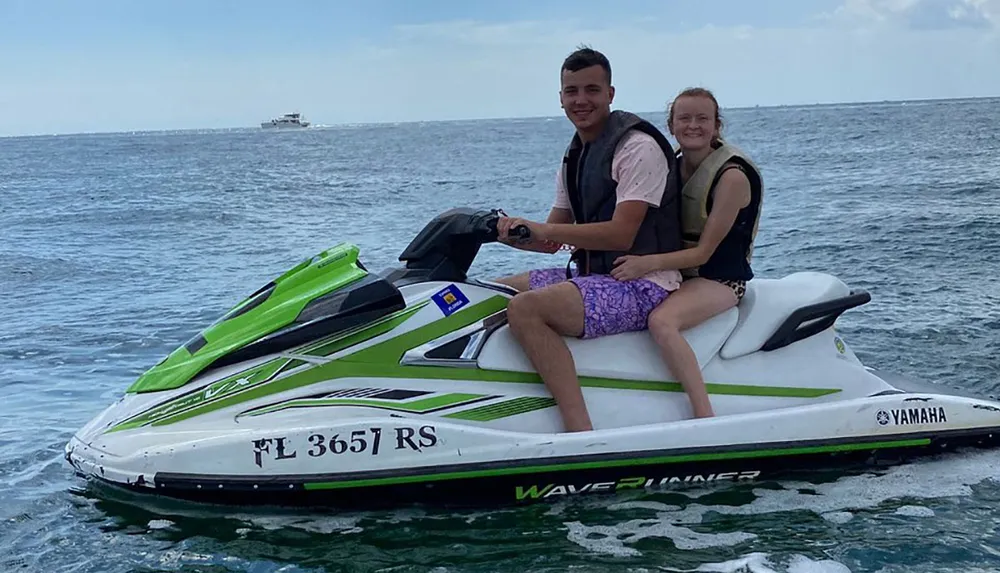 Two people are smiling and enjoying a ride on a Yamaha WaveRunner personal watercraft on a sunny day at sea with a distant boat on the horizon