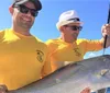 Three men are standing on a boat each proudly displaying their catch of fish with the water and some waterfront properties in the background