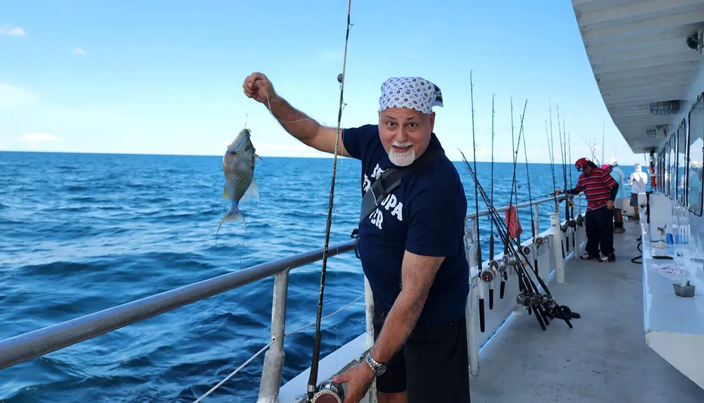 A man proudly shows off a fish he has caught while standing on a fishing boat with others fishing in the background