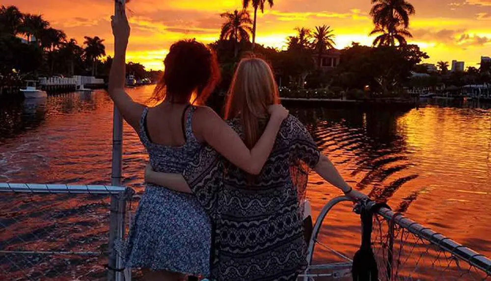 Two people stand on a boat enjoying a stunning sunset over a calm river silhouetted against a vibrant orange sky