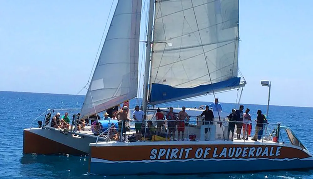 A group of people enjoys a sunny day on a catamaran named SPIRIT OF LAUDERDALE sailing on blue waters