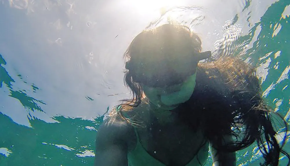 A person is taking a selfie while swimming underwater with sunlight filtering through the waters surface above them