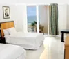 The image shows a modern beachfront bedroom with a large window offering a beautiful view of the ocean