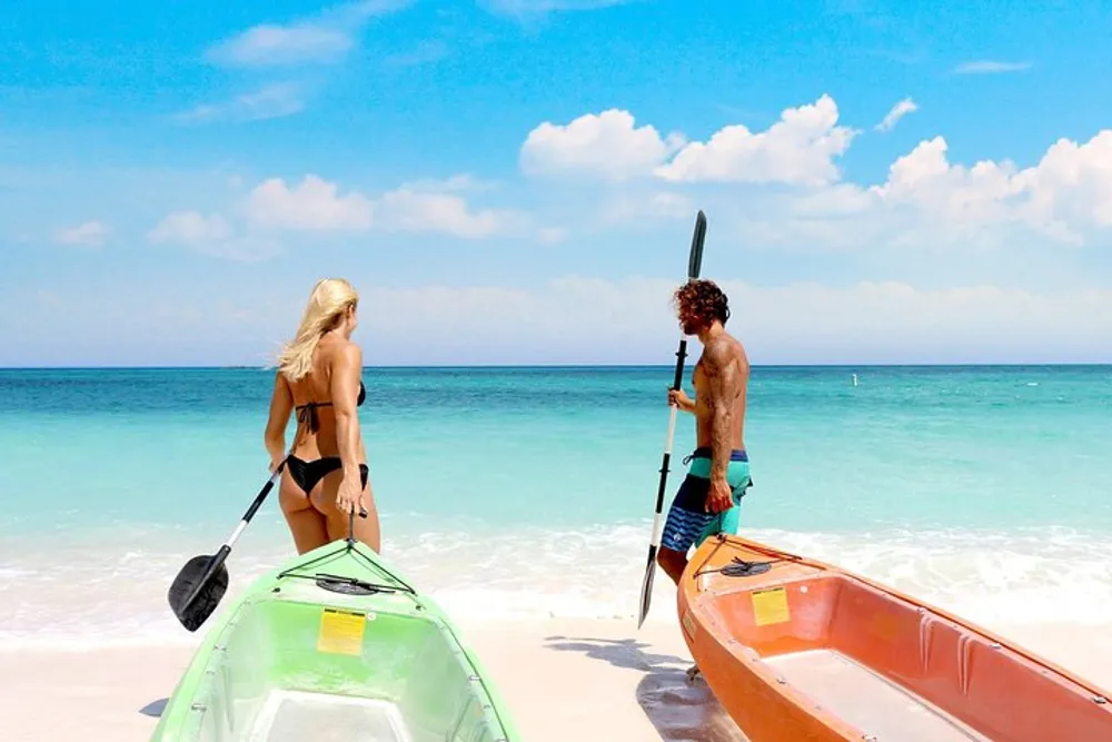 A man and a woman are standing by two kayaks on a beautiful tropical beach preparing to go paddling