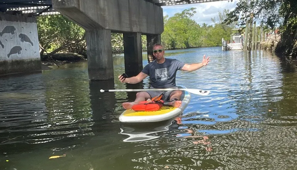 A person is relaxing on a paddleboard under a bridge spreading his arms with a serene expression on his face