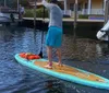 Three people are stand-up paddleboarding in a sunny waterway with boats and waterfront homes in the background