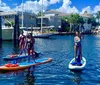 Three people are stand-up paddleboarding in a sunny waterway with boats and waterfront homes in the background