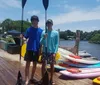 Two people are paddleboarding on a calm river with waterfront houses in the background