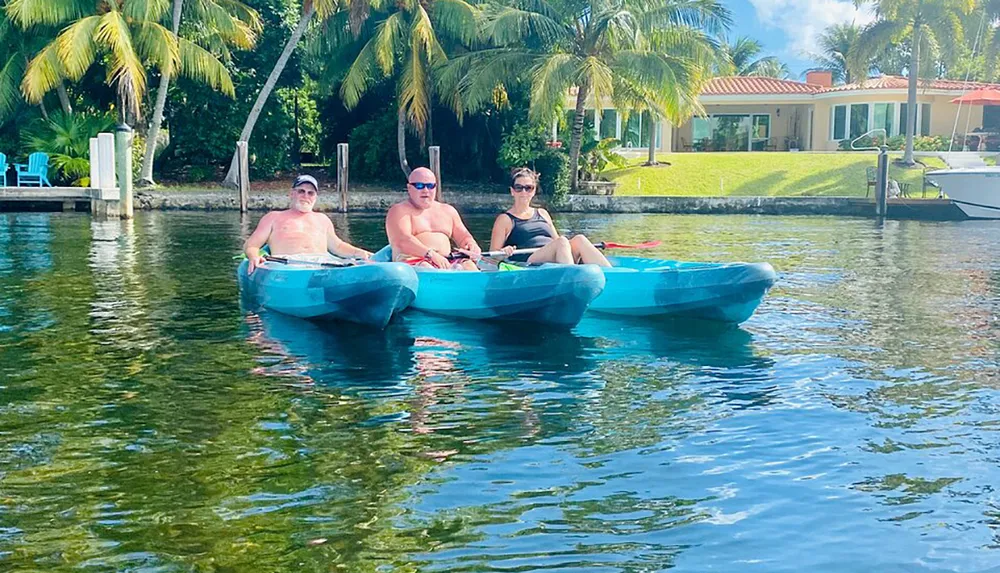 Three individuals are enjoying their time on a kayak in a scenic waterway surrounded by palm trees and waterfront properties