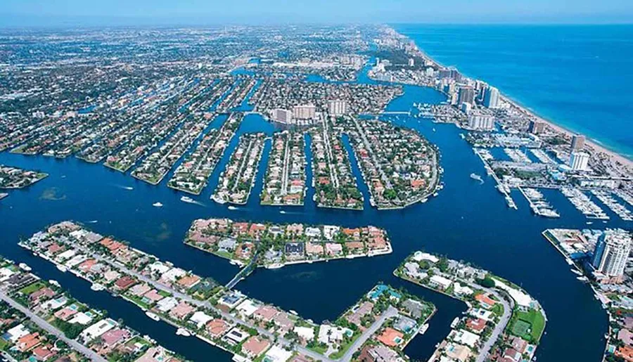 This is an aerial view of a coastal urban area featuring numerous canals and waterways with residential and commercial buildings closely packed along their banks, leading out to a larger body of water.