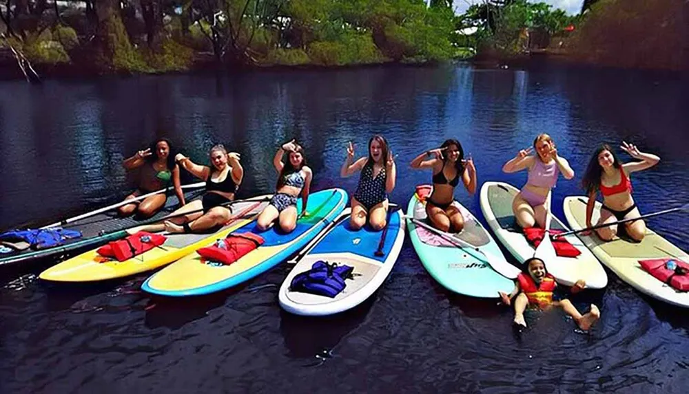 A group of people are enjoying a sunny day paddleboarding on calm water with some posing for a playful photo