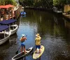 Two people are smiling and posing on stand-up paddleboards on a tranquil river surrounded by lush greenery