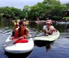 Two people are smiling and posing on stand-up paddleboards on a tranquil river surrounded by lush greenery