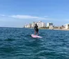 A person is paddleboarding on a calm sea with a view of a coastal city skyline in the background