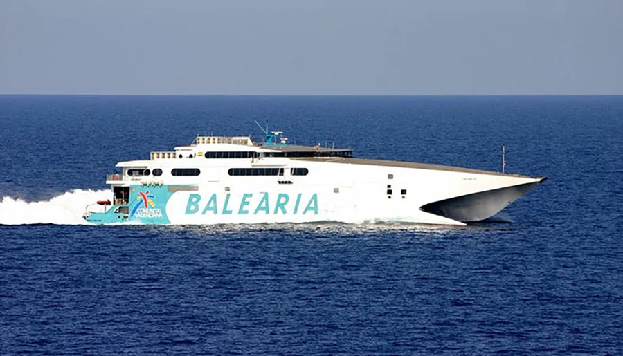 A high-speed ferry with the name BALEARIA on its side is cruising through blue waters.