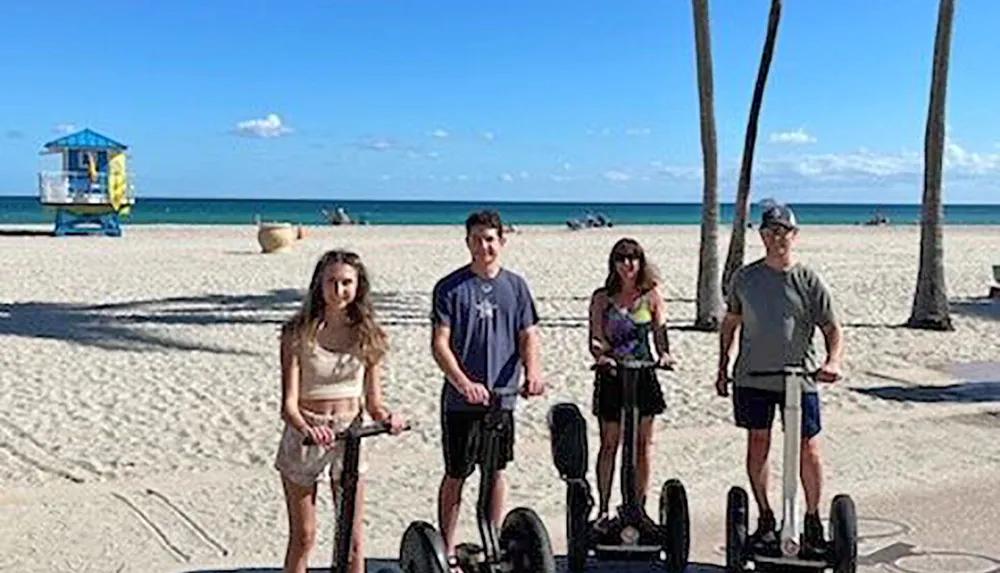 Four people are posing for a photo on a sunny beach each standing with a Segway