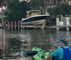 A group of smiling people are seated in colorful kayaks on calm water with two dogs also visible on the kayaks