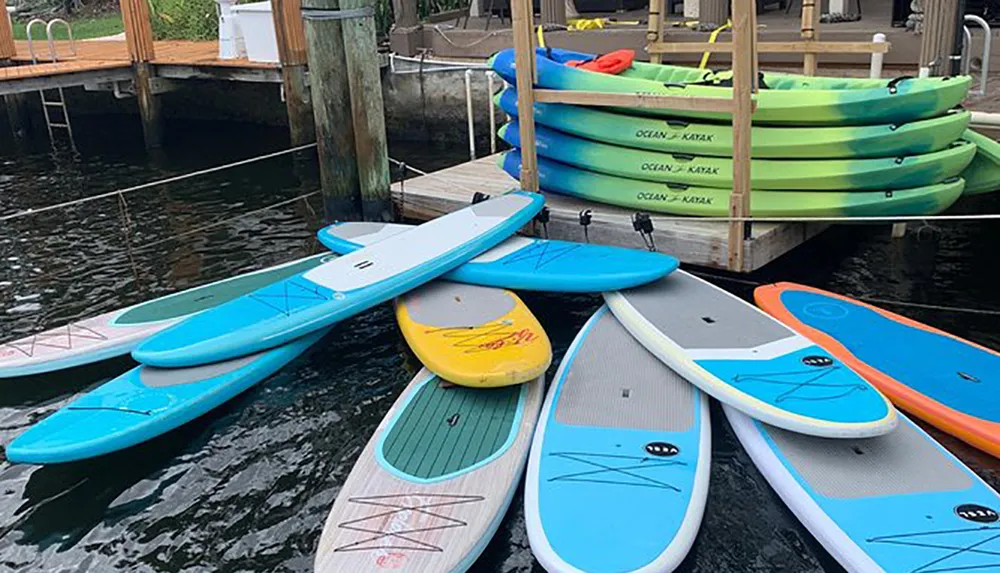 A variety of colorful paddleboards and kayaks are neatly arranged on a dock by the water