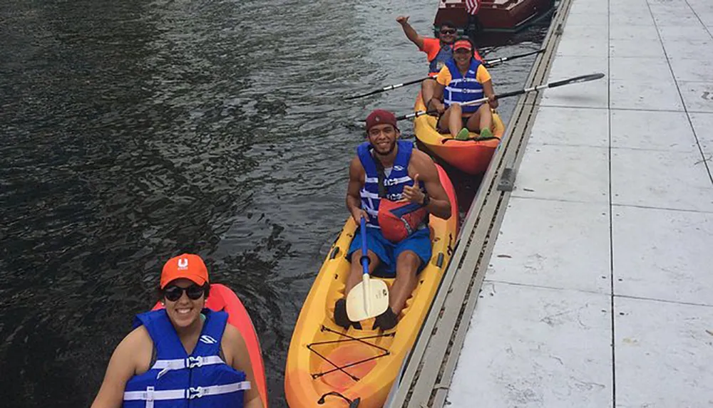 A group of people wearing life jackets is smiling and posing for a photo while sitting in colorful kayaks on the water