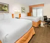A tidy hotel room with two queen-sized beds a work desk with a chair a flat-screen TV and decorative artwork on the wall