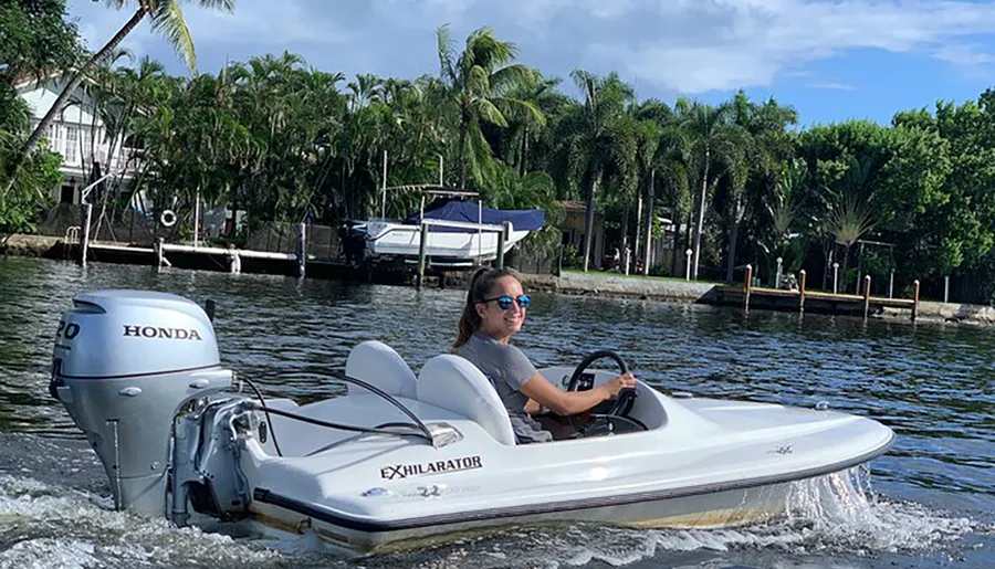 A person is driving a small motorboat on a waterway with tropical vegetation in the background.