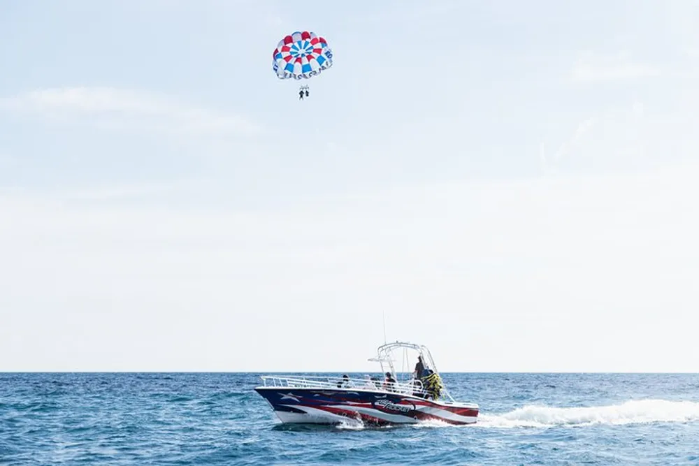 A speedboat is on the ocean towing a parasail with two people flying high above the water